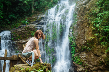 Fototapeta na wymiar Young woman enjoying tropical waterfall in Asia