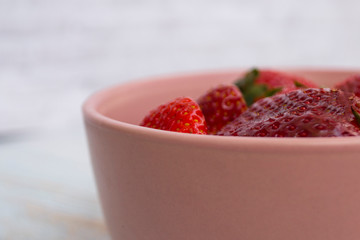Red strawberry in a pink bowl on a light background.