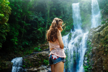Young woman enjoying natural bathing by the Tamaraw waterfall on background. Puerto Galera, Mindoro Island, popular tourist place of Philippines