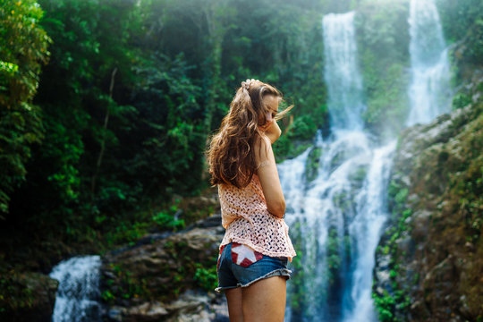 Young woman enjoying natural bathing by the Tamaraw waterfall on background. Puerto Galera, Mindoro Island, popular tourist place of Philippines