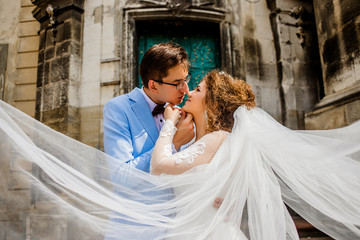 Stylish beautiful couple on the background of old stone church. Woman with lace veil.