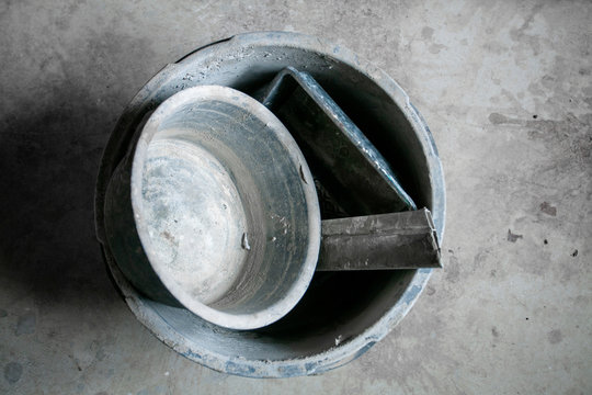 Construction bucket with dried mortar sluge on the concrete floor. Concept of repair and construction process. Finishing work at home. Rennovation and new interior.