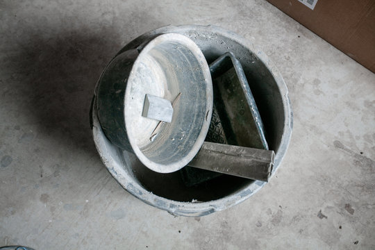 Construction bucket with dried mortar sluge on the concrete floor. Concept of repair and construction process. Finishing work at home. Rennovation and new interior.