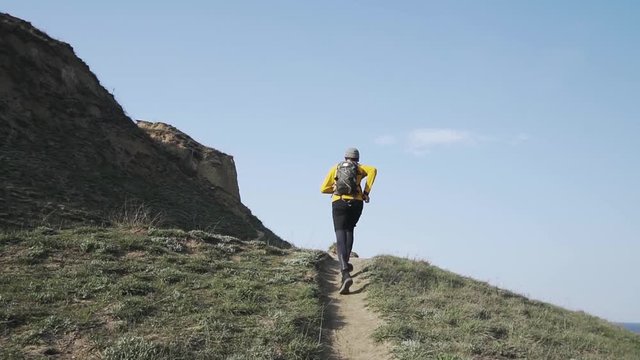 Young male trail runner with backpack training on the hill in sunny day 