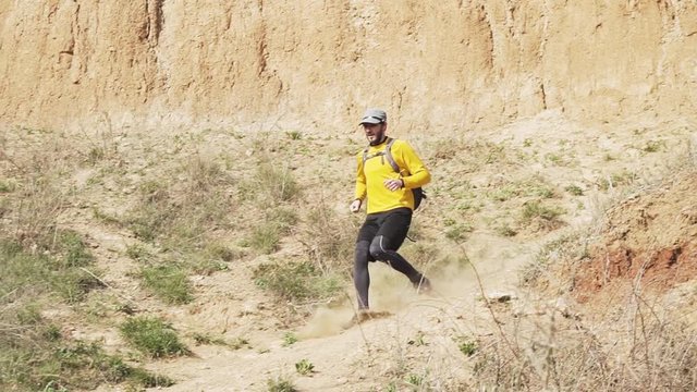 Young male trail runner with backpack training on the hill in sunny day 