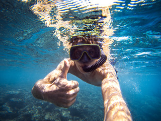 Selfie of young man snorkeling in the sea, thumb up