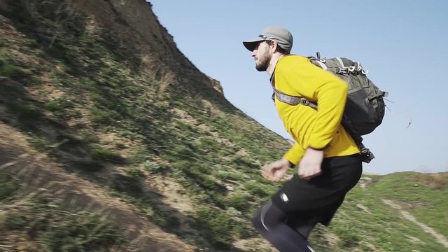Young male trail runner with backpack training on the hill in sunny day 