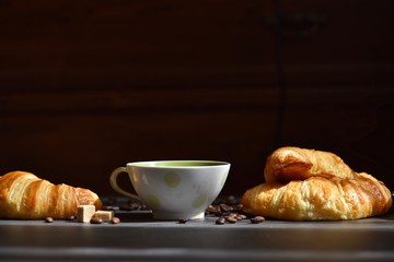 Coffee composition. Cup of coffee, croissants, sugar slices on a dark background 
