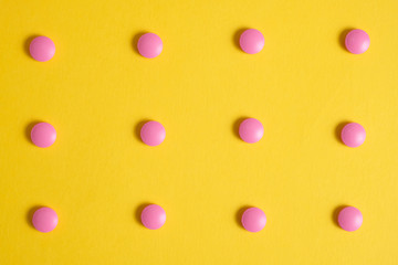 Neatly laid out pink pills on a yellow background. Background image.
