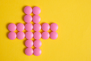 Cross of pink pills on a yellow background. Concept of help from drugs and other medicines.