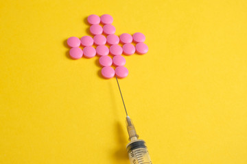 Cross of pink pills on a yellow background with a syringe. The concept of the required number of drugs.