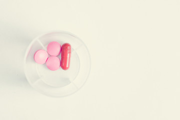 The concept of a daily dose of medicine for maintaining health of pink pills and capsules in a plastic container on a white background. Toned.