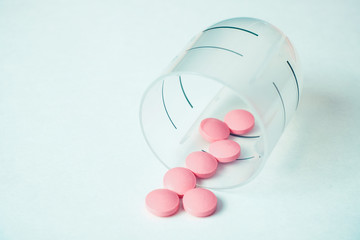 The concept of a daily dose of medicine for maintaining health from pink pills in a plastic container with a shattered container on a white background.