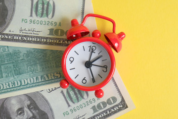 The concept of the start of business investment. A red vintage clock stands on one hundred US dollar bills on a yellow background.