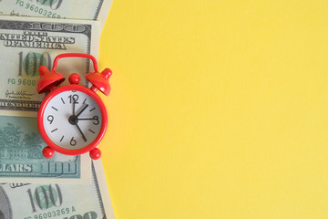 The concept of the start of business investment. A red vintage clock stands on one hundred US dollar bills on a yellow background. Place for text.