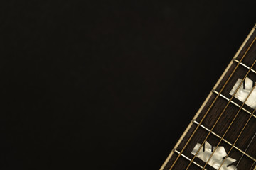 Close-up of an acoustic guitar neck in the right-down corner on black background