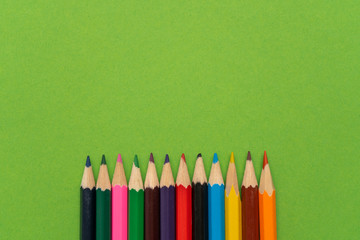 A rainbow of colored pencils for drawing and art down on a green background. Top view