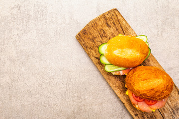 Homemade sandwich in bun. Salami, dried pork, tomato, cucumber, cheese ingredients. On wooden board and stone background, top view