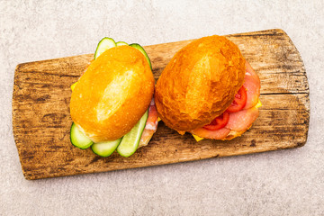Homemade sandwich in bun. Salami, dried pork, tomato, cucumber, cheese ingredients. On wooden board and stone background, top view