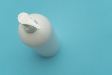 Close-up of a dispenser of white plastic bottle of liquid cosmetic(soap, shampoo, lotion), that stand on the left on a blue background. Top view