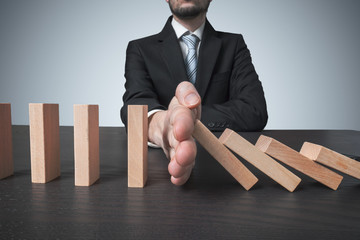 Intervention concept. Man stops falling domino with hand.
