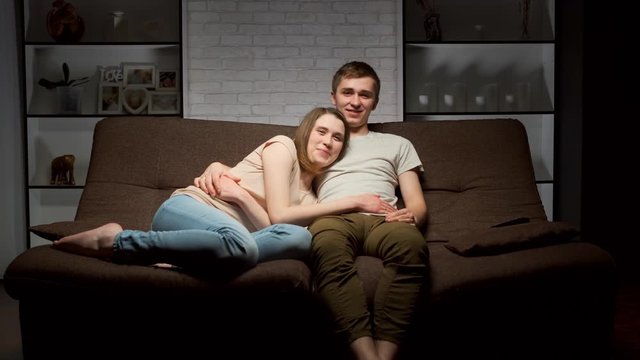guy and girl are watching TV and smiling.