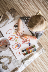 Little girl draws and decorates Easter eggs with water colors