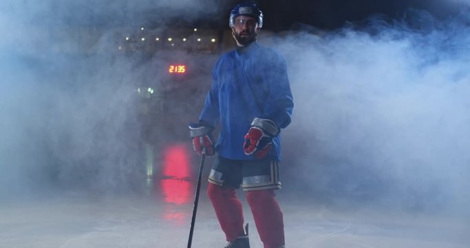 Professional hockey player with a stick and a puck moves on Luda in skates and helmet on a dark background and smoke. Dribbling with the puck of a young man on the ice arena