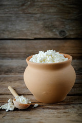Cottage cheese in brown rustic clay pot and wooden spoon.