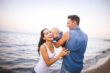beautiful young family on vacation with baby. The father holds the blonde girl in her arms, and the brunette's mother hugs her husband. The concept of a family beach holiday summer near the sea