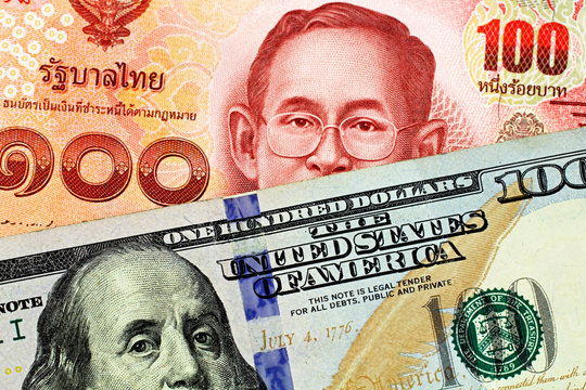 A close up imgae of a red one hundred Thai baht with an American one hundred dollar bill in macro