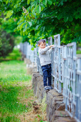 Naklejka na ściany i meble a boy in a beige knitted sweater walks along an iron gray fence