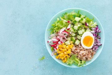 Buddha bowl with boiled egg, rice and vegetable salad of fresh lettuce, radish, cucumber, corn, onion and sesame seeds and chickpea sauce