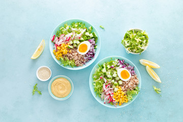 Fototapeta na wymiar Buddha bowl with boiled egg, rice and vegetable salad of fresh lettuce, radish, cucumber, corn, onion and sesame seeds and chickpea sauce