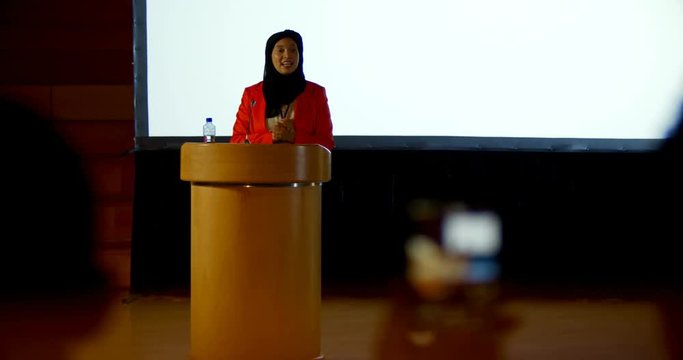 Mature Caucasian hijab businesswoman speaking at podium in auditorium 4k