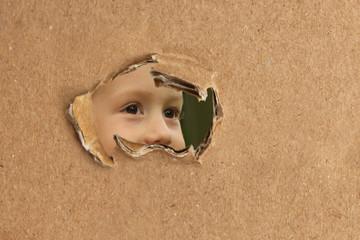 baby spying, peeking out of a hole in cardboard, the concept of shadowing