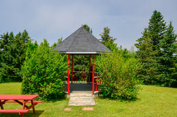 Park with Gazebo and bench, painted red, with cut grass and pine trees in Nova Scotia Canada 