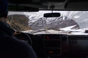 Inside view from the interior of a vehicle to the front window, with a winter route on the background with snow on the shoulder. The driver is in a blur and the interior is dark, with copy space