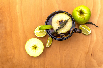 Fruit tea concept. Fresh lime and apple, dry herbs. Glass brown cup on a wooden background, top view