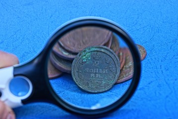 a big magnifier and a bunch of old brown copper coins on a blue table