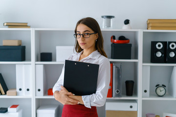 portrait of young beautiful brunette businesswoman work in office hold binder in arms