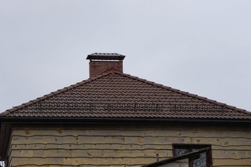 part of a wooden house with a window and a brown tiled roof with a chimney against a gray sky