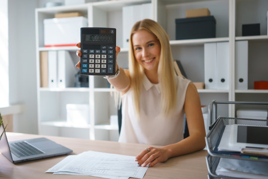 young blond pretty woman sit at table in office use calculator
