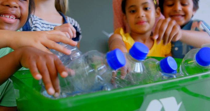 African American girl and boy schoolkids putting bottles in recycle container at desk in classroom 4k