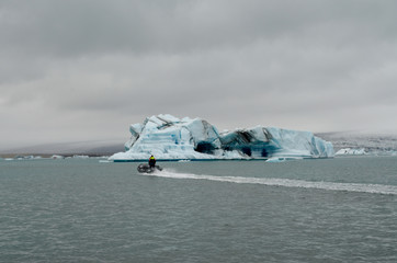 Man in motor boat (zodiac) cruising across Iceland Glacier Lagoon with Iceberg in background