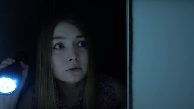 Attractive blond-haired woman holding flashlight and opening a door, checking a room in the darkness. Nightmare of young woman that feels fear and scare.