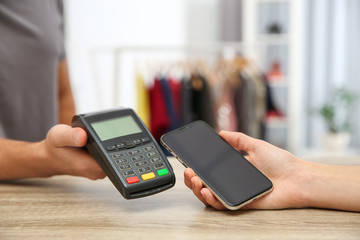 Woman using payment terminal with smartphone in shop, closeup. Space for text
