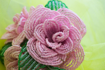 Rose made from beads, pink. On a yellow blurred background.