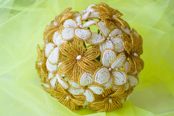 Wedding bouquet golden and white flowers from beads. On a yellow blurred background.