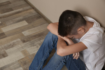 Upset boy sitting on floor at wall. Space for text
